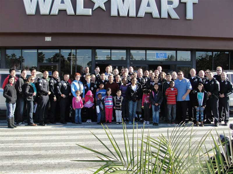 A large group of adults and children pose for a photo outside a Walmart store, standing on the crosswalk near the entrance.