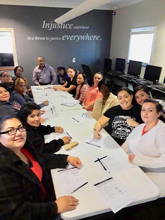 A group of people sit around a table in a meeting room with papers and pens; a quote about justice is displayed on the wall behind them.