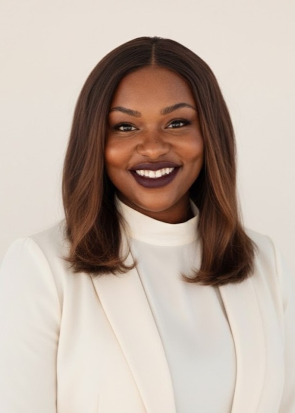 A woman with straight, shoulder-length hair wearing a white blazer and high-neck top smiles at the camera against a plain background.