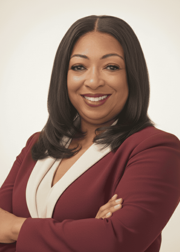 A woman with straight dark hair in a maroon blazer and white blouse stands with arms crossed, smiling at the camera against a plain light background.