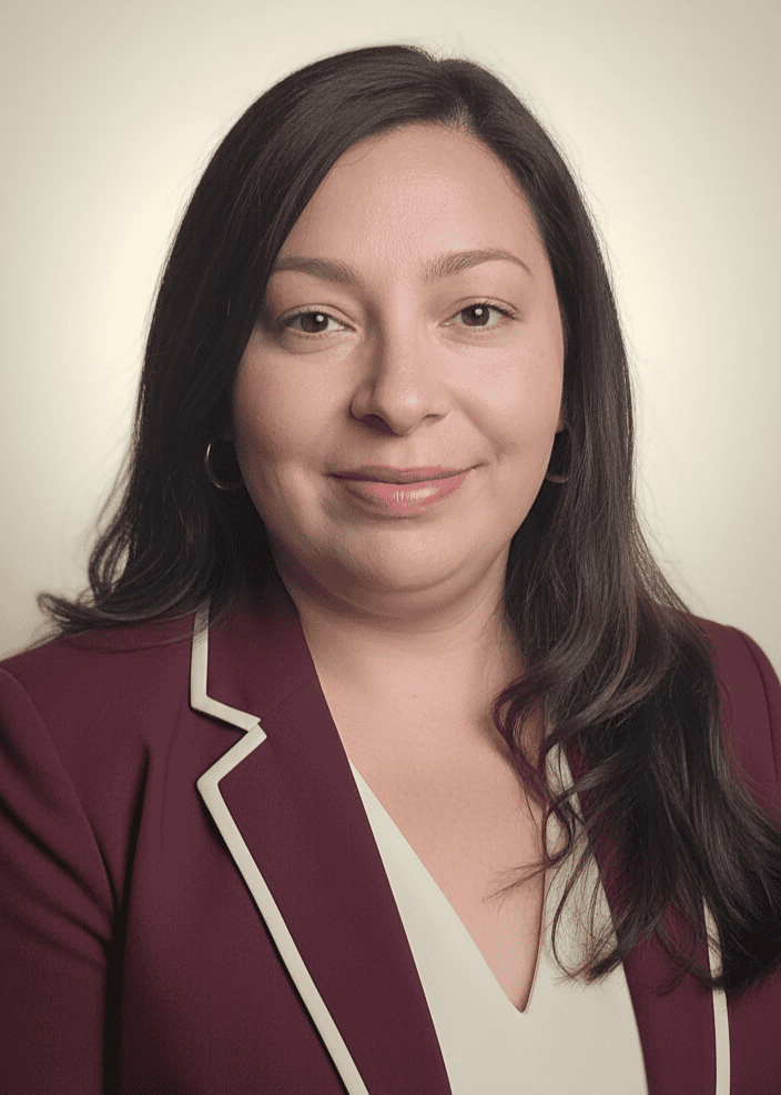 A woman with long dark hair wearing a maroon blazer with white trim and a white top, posing for a professional portrait against a neutral background.