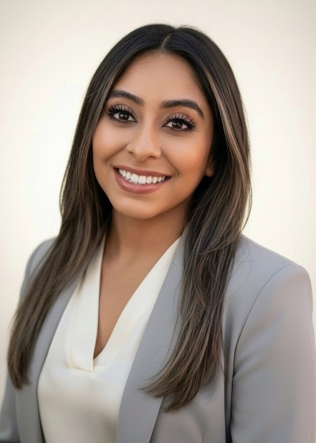 Woman with long straight hair wearing a light gray blazer and cream blouse, smiling in a professional portrait against a neutral background.